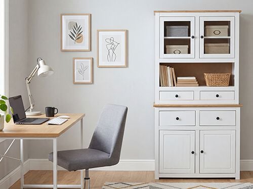 Interior scene showcasing a white cabinet, wooden desk, and office chair with botanical prints on the wall. The cabinet is filled with decorative items and books, and a laptop and plant are visible on the desk. Click to see the products in the collection.